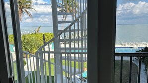 En balkong med ett vitt räcke, utsikt över havet och en palm.