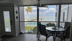 En täckt uteplats med utsikt över en pool och havet, med ett bord och stolar.