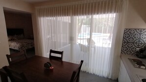 A room with a bed, a dining table with chairs, a kitchen area, and a large window with sheer curtains. - Marysol edificio blanco depto 1 Isla Mujeres (Isla Mujeres)