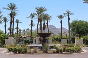 A landscaped area with a central fountain, palm trees, and a mountain in the background. - The Artisan Villa | 3BR Legacy Villa (La Quinta)