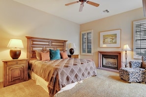 A bedroom with a bed, nightstands, a lamp, a fireplace, and a ceiling fan.