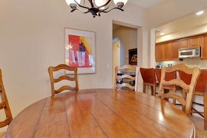 A dining area with a round wooden table and chairs, a chandelier, and wooden cabinets in the background.