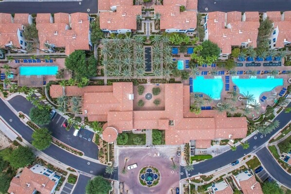 An aerial view of a resort with multiple buildings, swimming pools, and a central circular plaza.