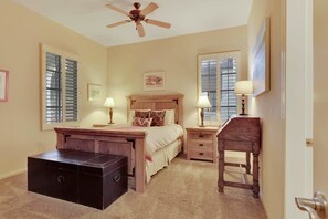 A bedroom with a bed, bedside tables, a dresser, a ceiling fan, and a window with shutters.