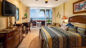 A bedroom with a bed, a TV, a ceiling fan, a desk, and a view of the beach. - Three Steps Onto the Most Beautiful Beach in Cozumel (cozumel)