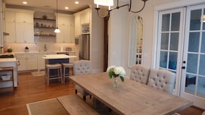A kitchen with white cabinets, a central island, and bar stools. There is a dining table with a vase of flowers.