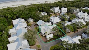 An aerial view of a coastal residential area with houses, a beach, and dense vegetation.