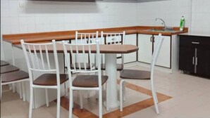 Una cocina con una mesa de comedor, sillas blancas, un armario negro y una estantería con plantas.