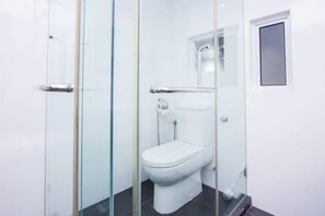 A bathroom with a glass shower enclosure, a white toilet, and a small window. - Maritime Penang by SYNC (George Town)