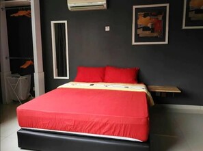 A bedroom with a large bed, a small bedside table, a wardrobe, and an air conditioning unit on the wall.