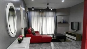 Un salon moderne avec un canapé rouge, une table d’appoint blanche ornée de fleurs, un téléviseur posé sur un meuble en bois et un sol en marbre.