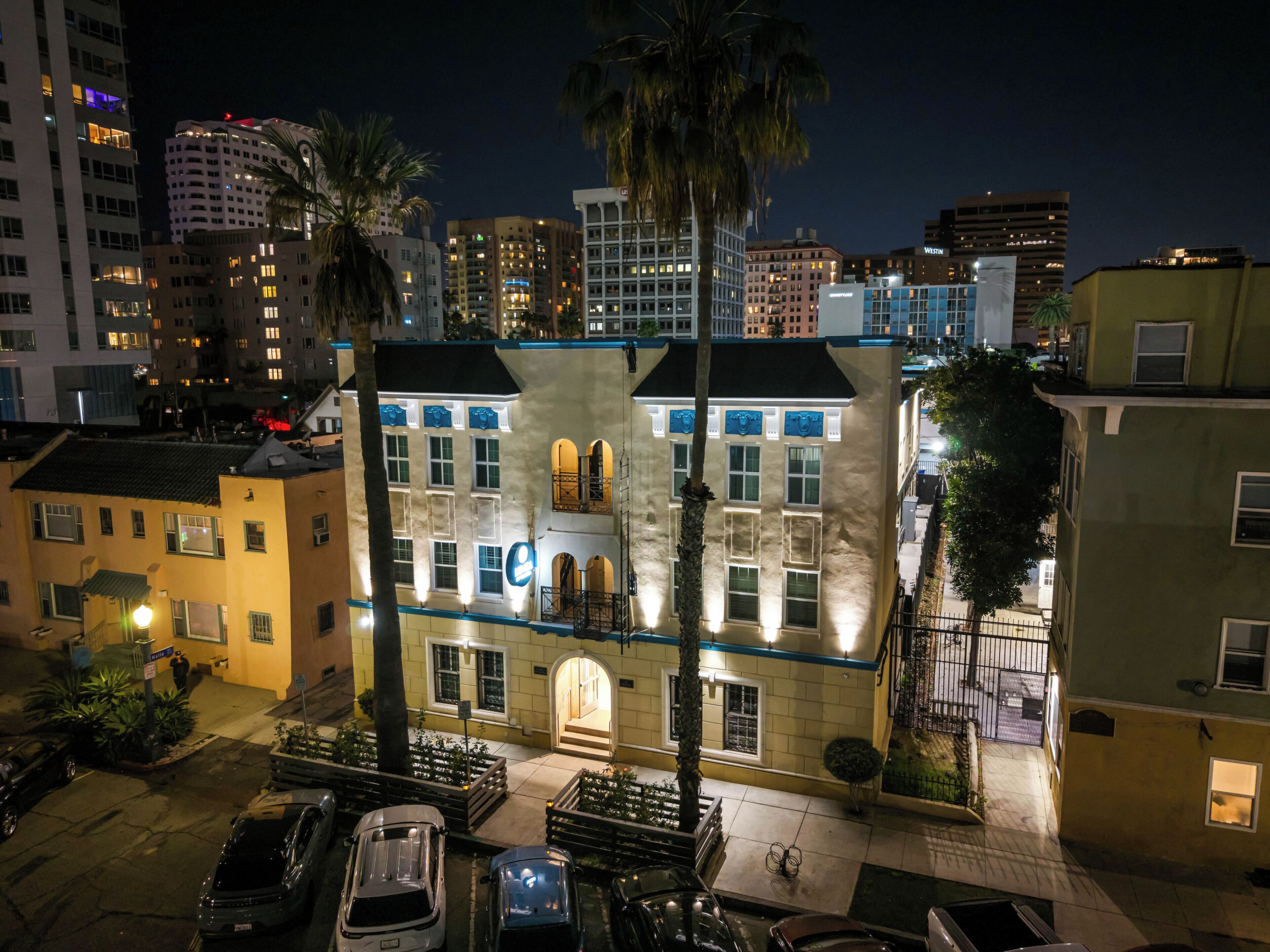 Un edificio de varios pisos con balcón, zona de estacionamiento y vista a la calle de noche.