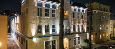 Un hotel de varios pisos con un diseño arquitectónico clásico, que presenta un balcón y una fachada bien iluminada.