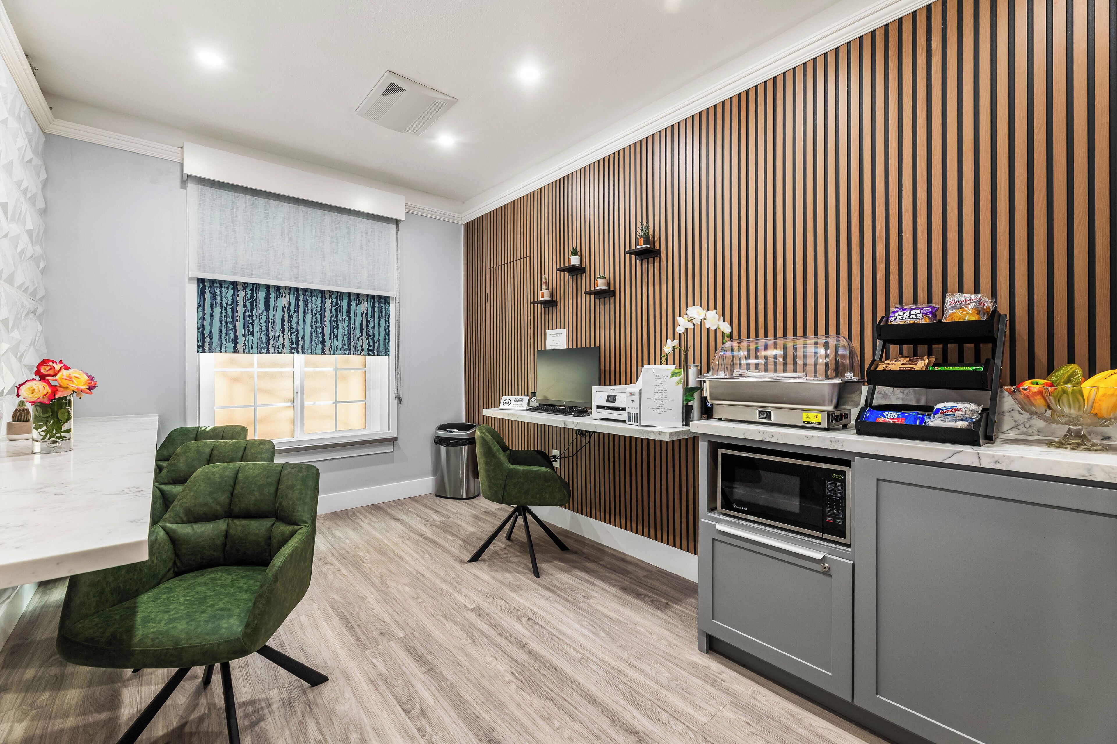 A modern kitchen with a wooden accent wall, a dining area with green chairs, and a window with curtains.