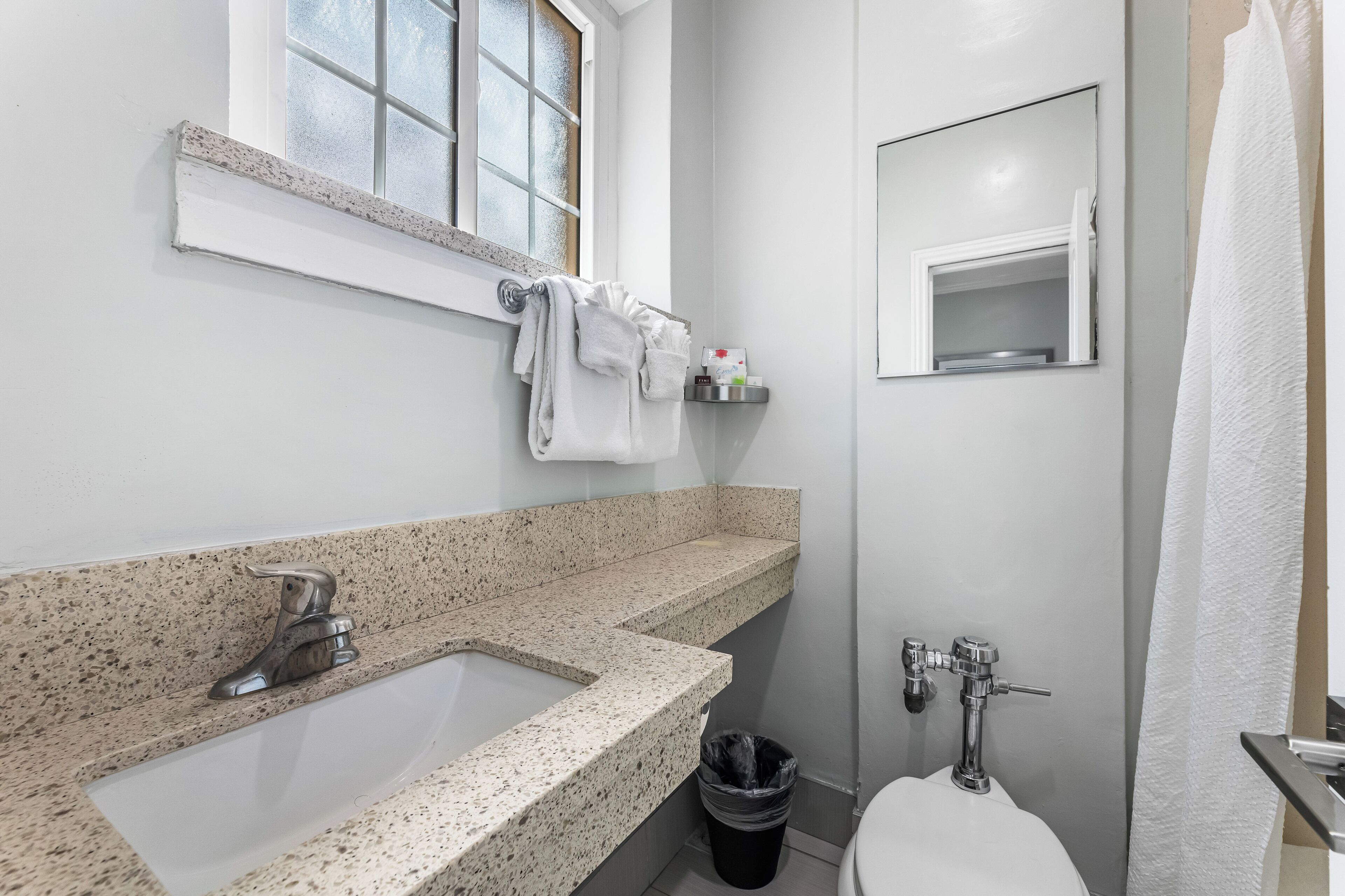 A bathroom with a granite countertop sink, a mirror, a towel rack, and a toilet.