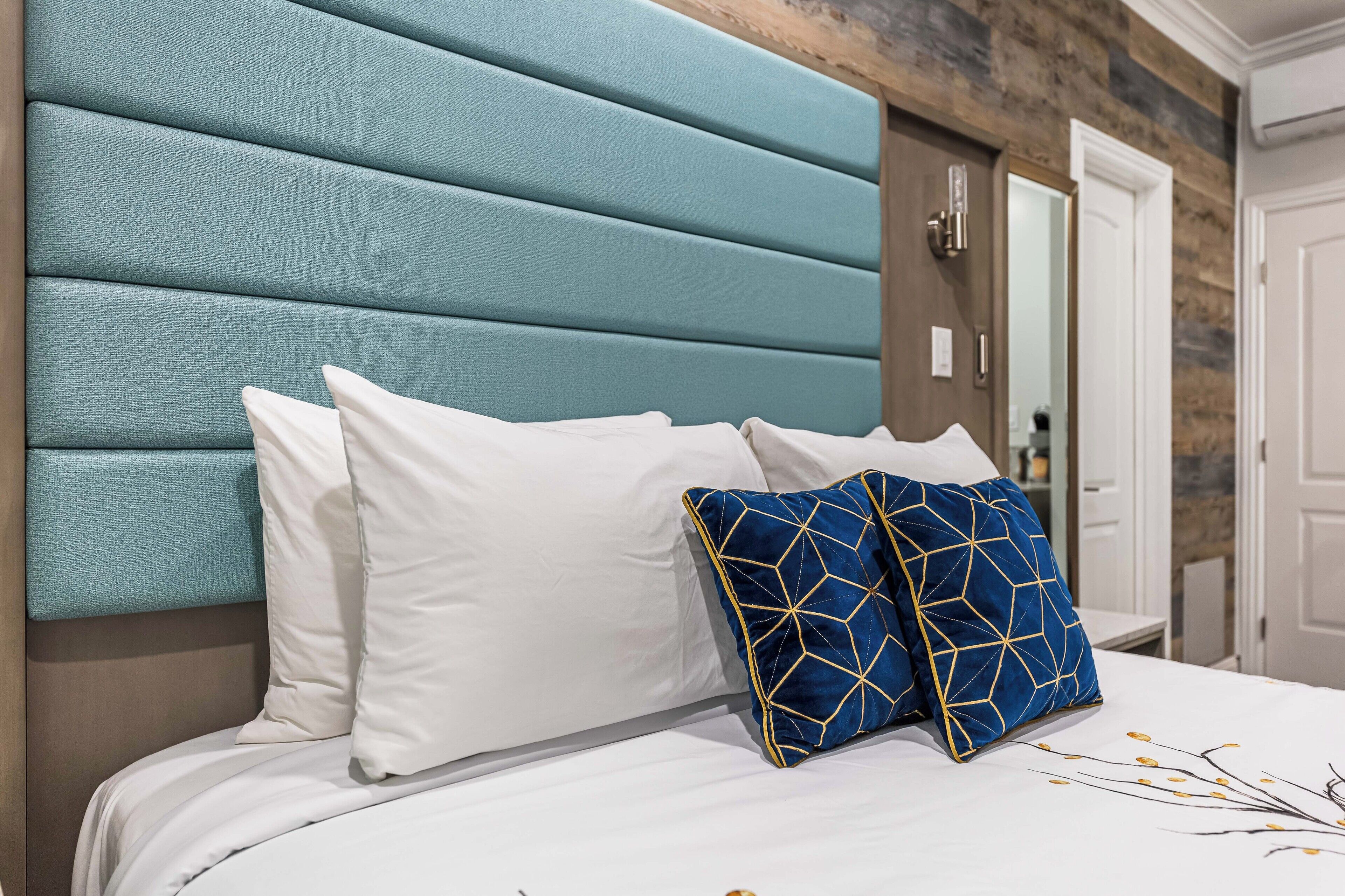 A bed with a teal upholstered headboard, white and blue patterned pillows, and a white bedspread with a branch design.