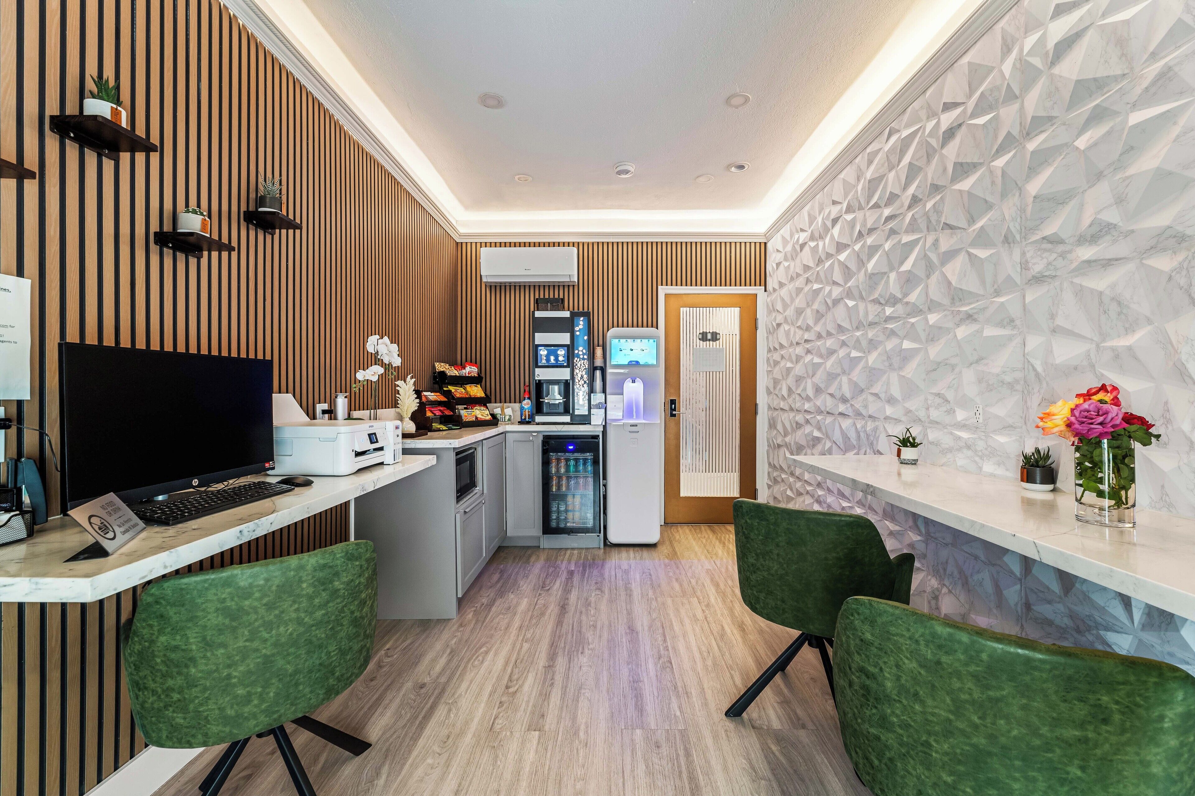 Una moderna zona de recepción con un panel de madera, mostrador de recepción, refrigerador, microondas y una pequeña sala de estar con sillas verdes.