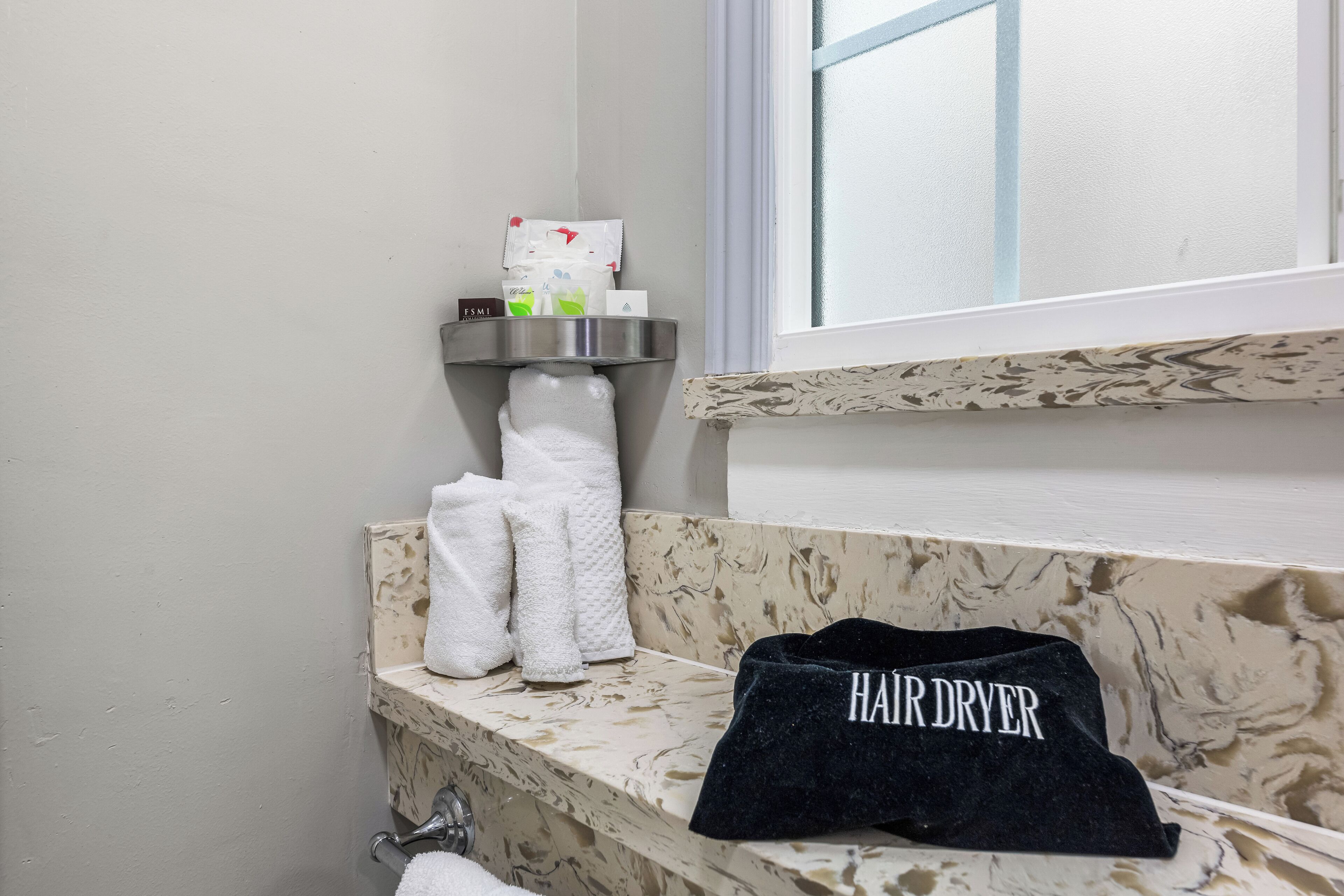 A bathroom with a marble countertop, a towel rack with multiple towels, a hair dryer, and toiletries on a shelf.