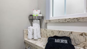 A bathroom with a marble countertop, a towel rack with multiple towels, a hair dryer, and toiletries on a shelf.
