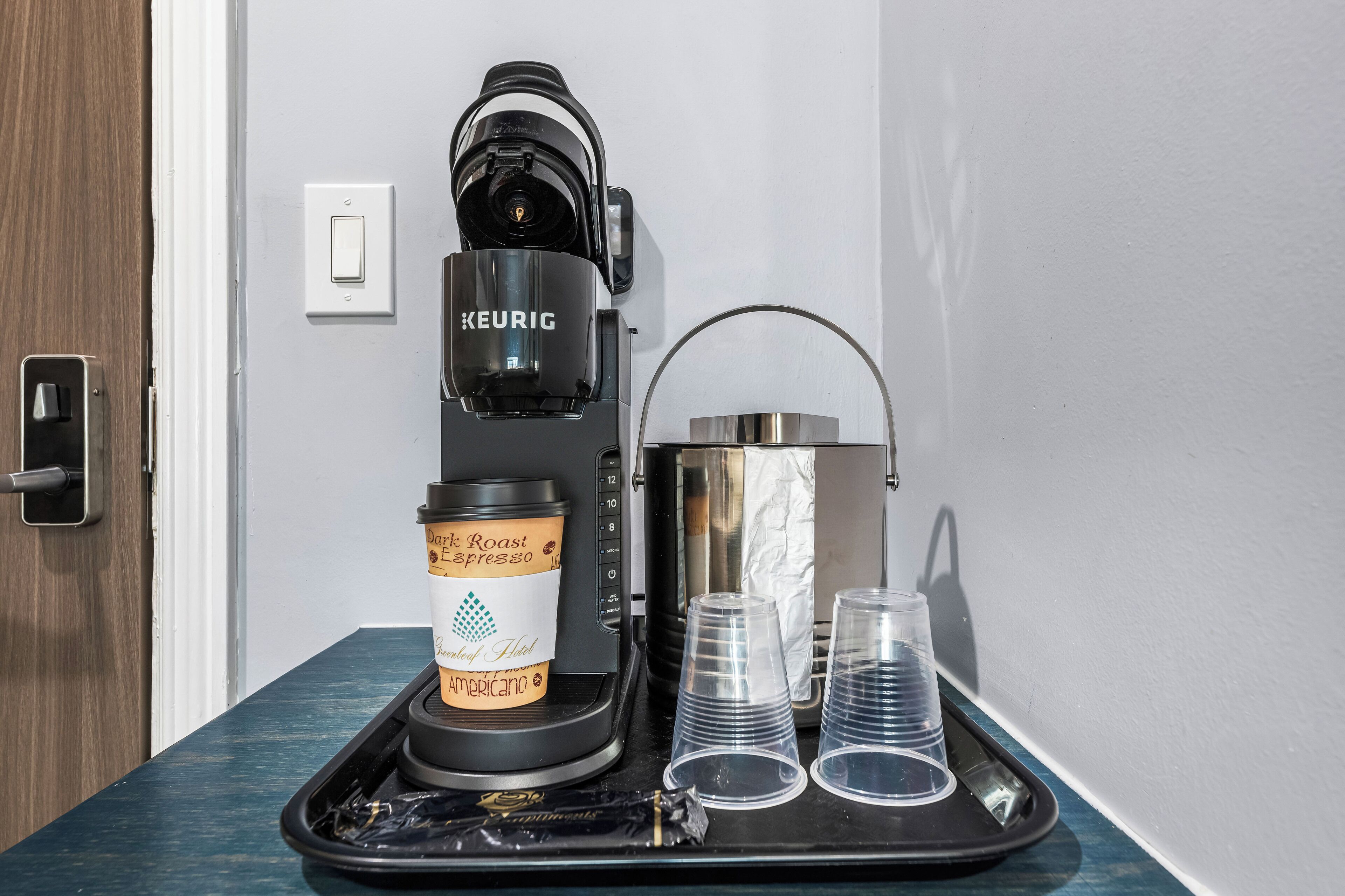 A Keurig coffee machine, a coffee pod, and plastic cups on a tray.