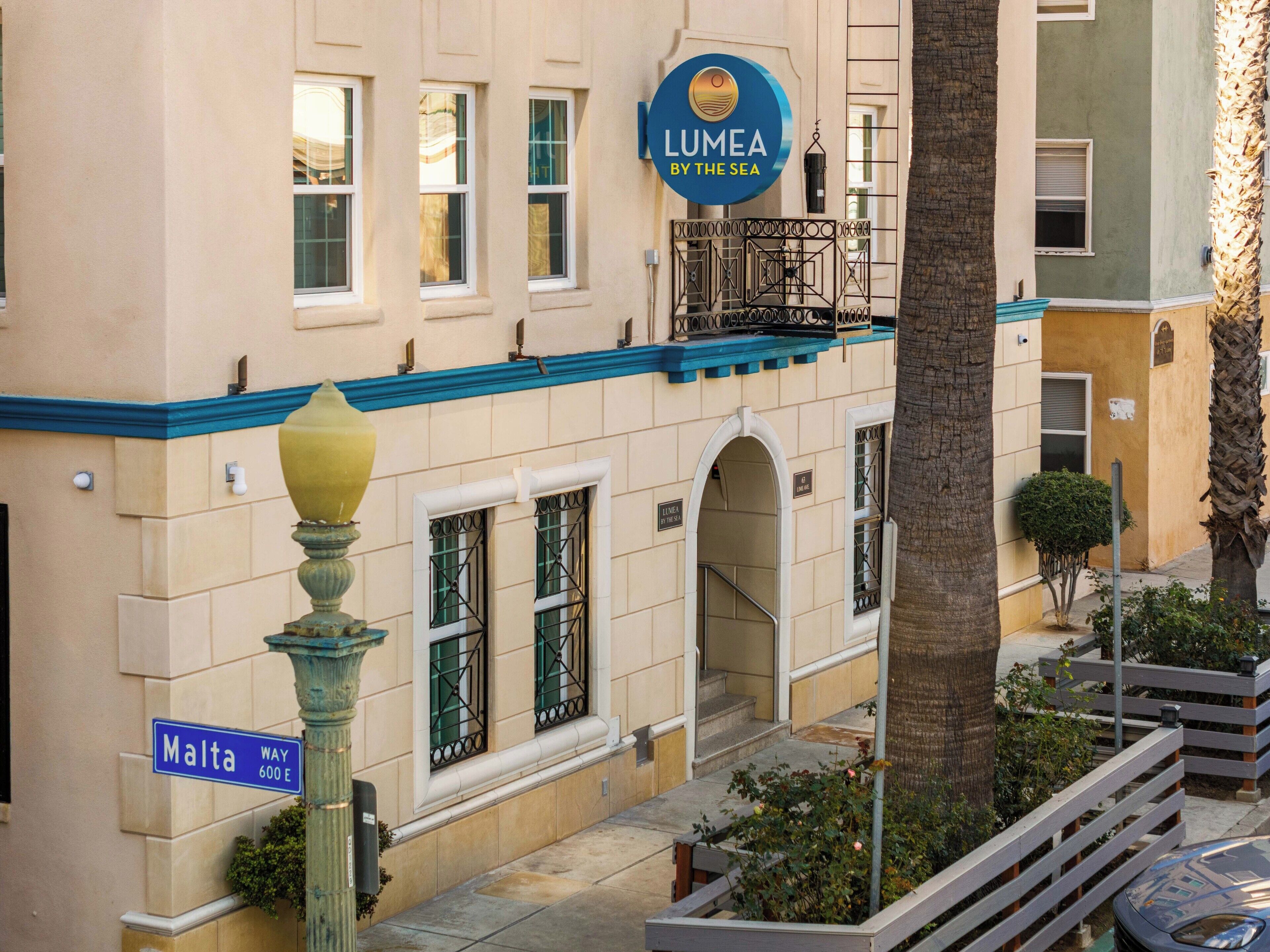 Un hotel llamado 'Lumea by the Sea' con un letrero, una señal de calle que indica 'Malta Way 600 E' y vista de la fachada y la entrada del edificio.
