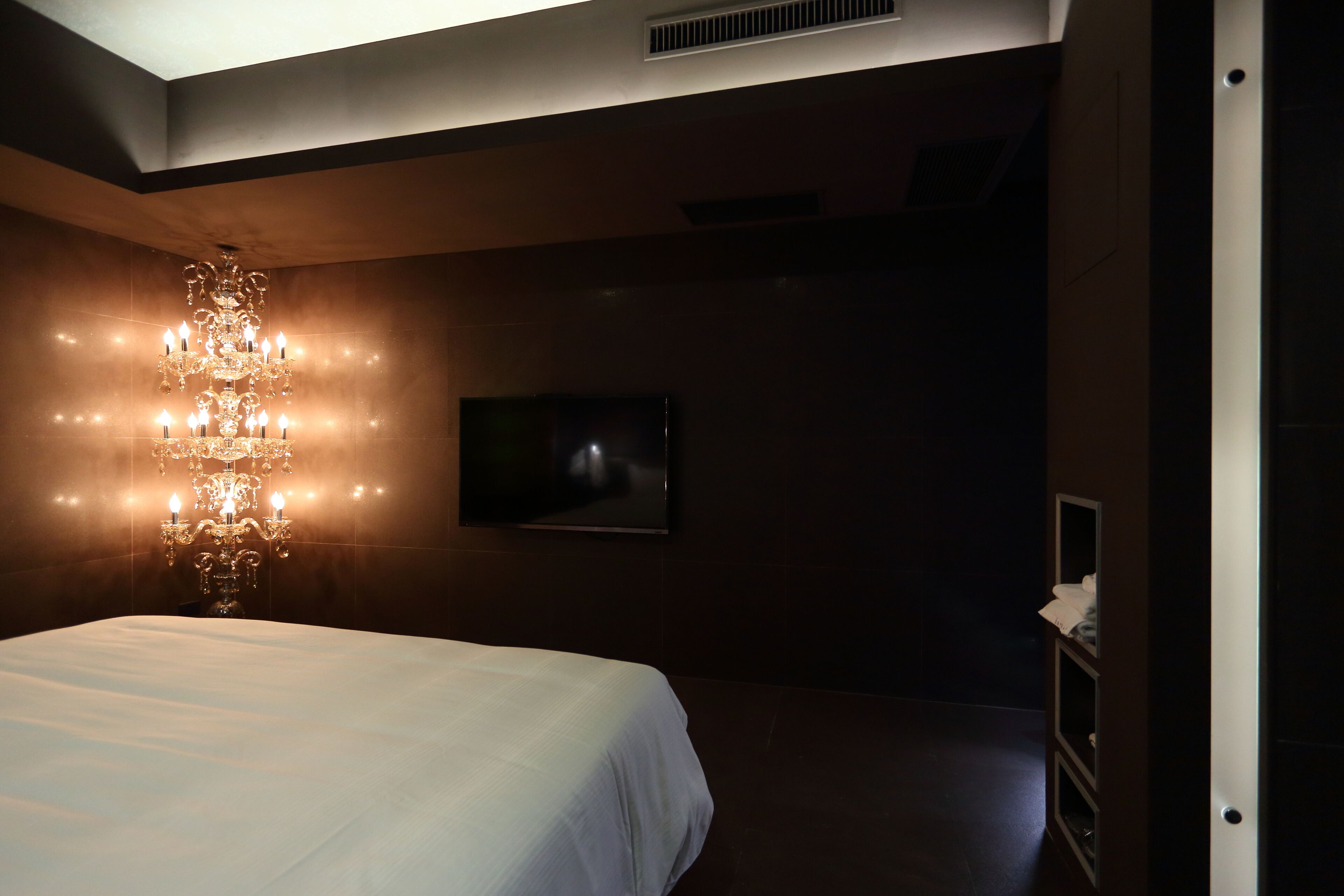 Une chambre à coucher avec un grand lit, un lustre, un téléviseur à écran plat et une armoire.