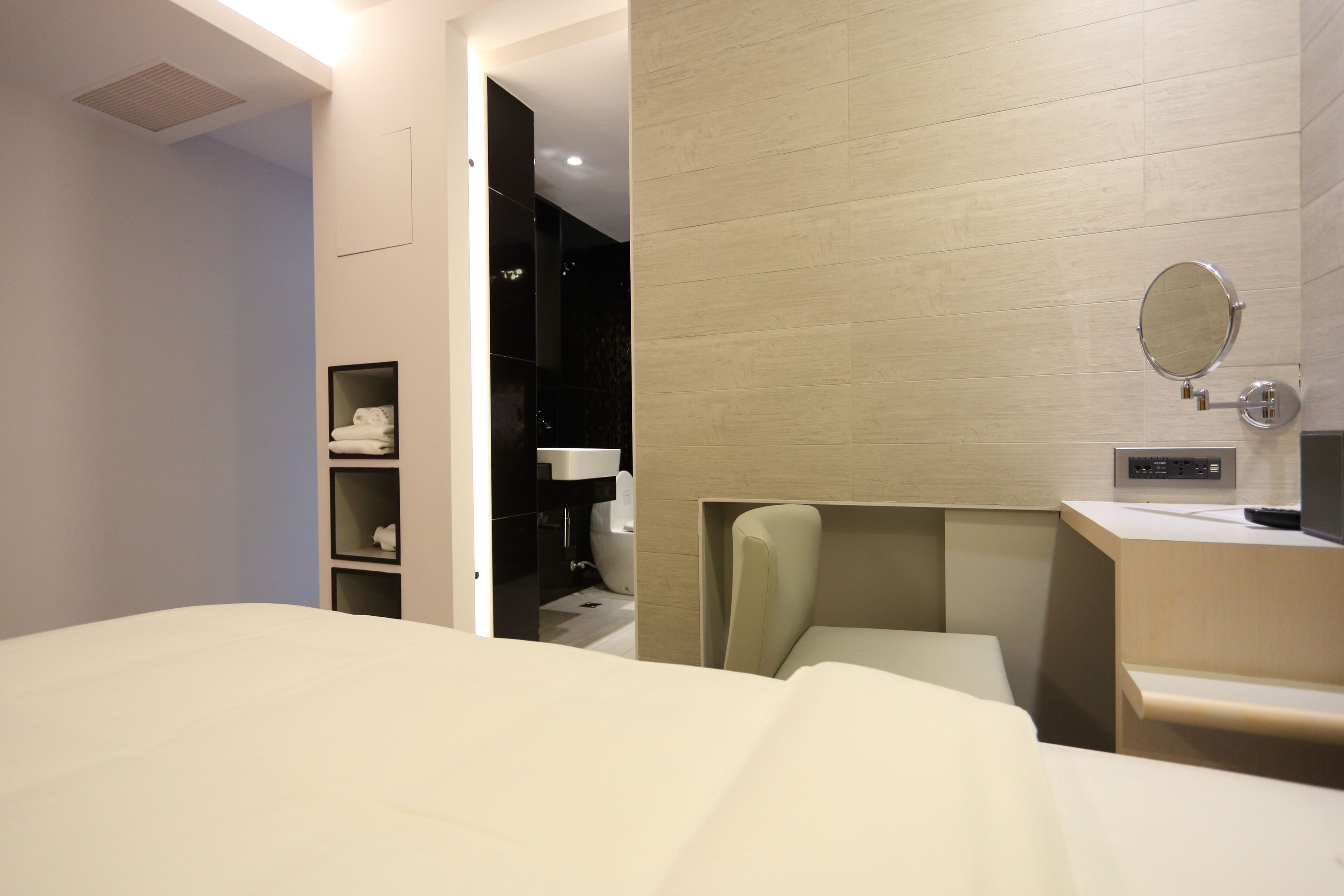 Habitación de hotel con cama, mesita de noche, una silla, espejo y baño pequeño con lavabo e inodoro.