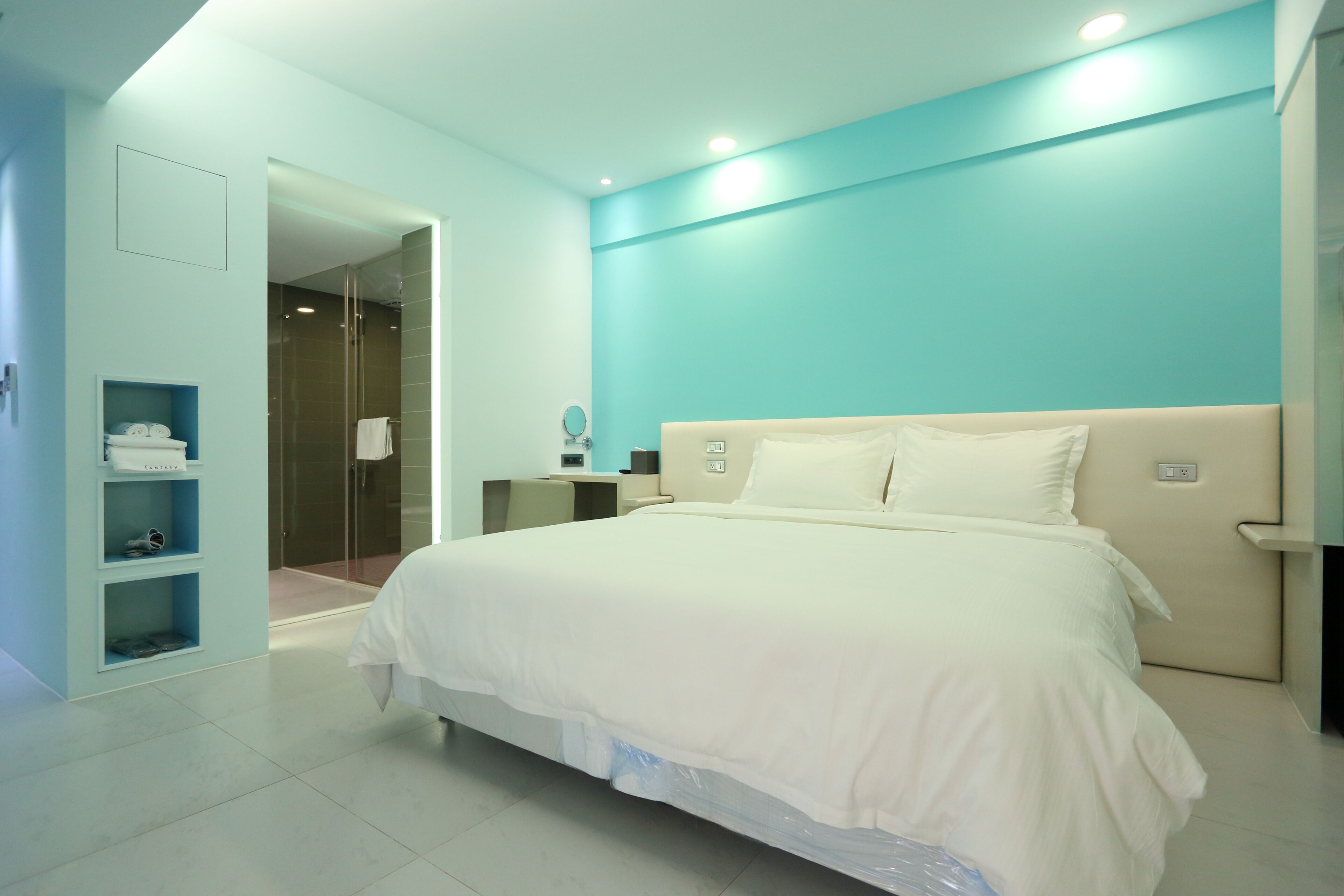 Una camera d'albergo moderna con un letto grande, un cabina armadio e un bagno con doccia in vetro.
