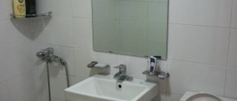 Une salle de bain avec un lavabo blanc, un miroir, des toilettes et une douche.