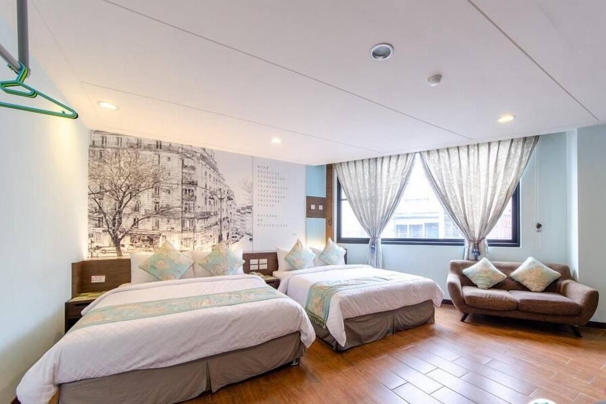 A hotel room with two beds, a sofa, a large wall mural, and a window with curtains.