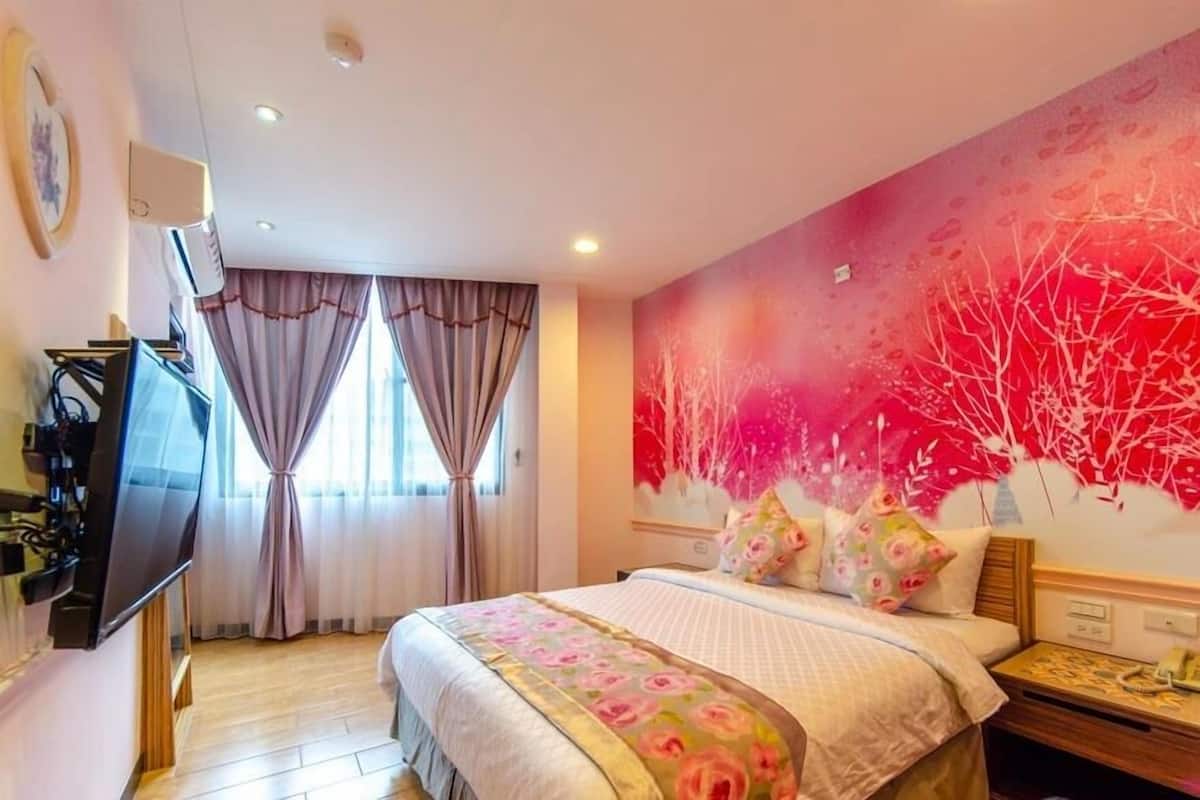 A hotel room with a bed, curtains, a wall mural, a flat-screen TV, and a wooden floor.