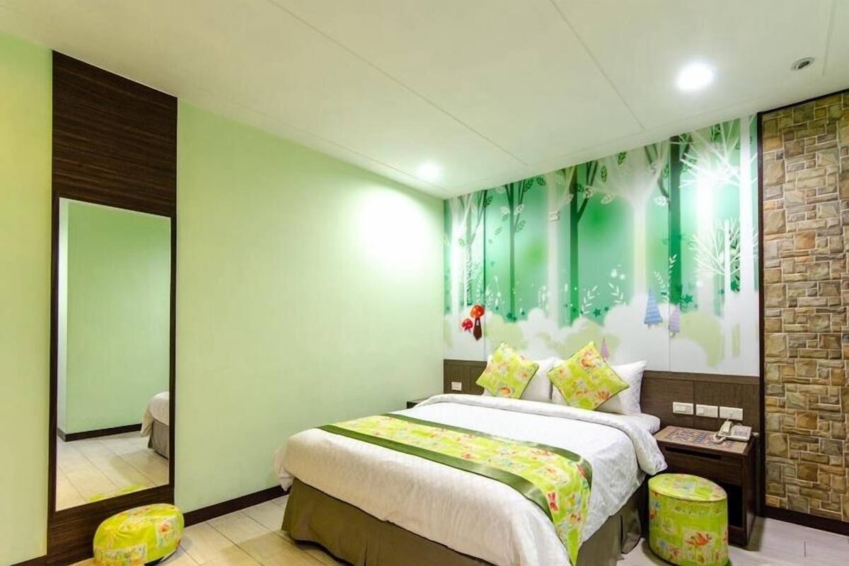 A bedroom with a bed, a nightstand, a mirror, and a wall with a nature-themed mural.
