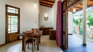 A dining area with a wooden table and chairs, a kitchen area with a sink and countertop, and large windows with a view of greenery. - Udawalawe Ayurvedic Resort (Rankethgama)