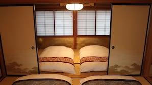 A traditional Japanese room with sliding doors, two beds with patterned bedding, and a ceiling light. - K's Villa Hida-an (Takayama)