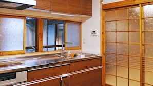 A kitchen with wooden cabinets, a stainless steel sink, and a sliding glass door with frosted glass panels. - K's Villa Hida-an (Takayama)