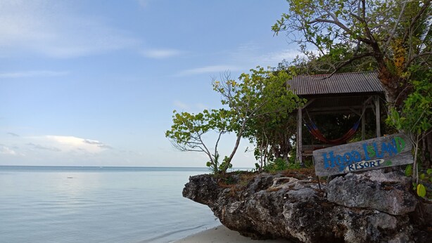 Een houten bordje voor Hoga Island Resort op een rotsachtige uitstulping aan een strand.