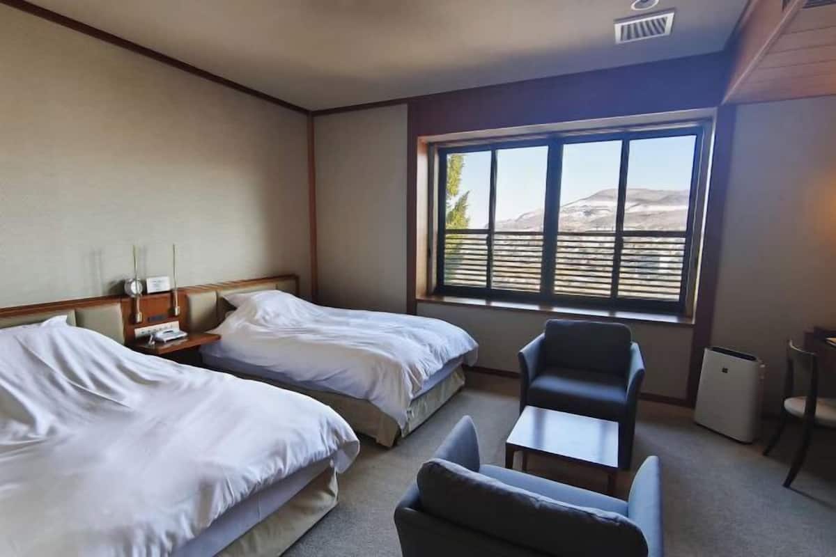 A hotel room with two beds, a chair, a small table, and a window with a view of mountains.