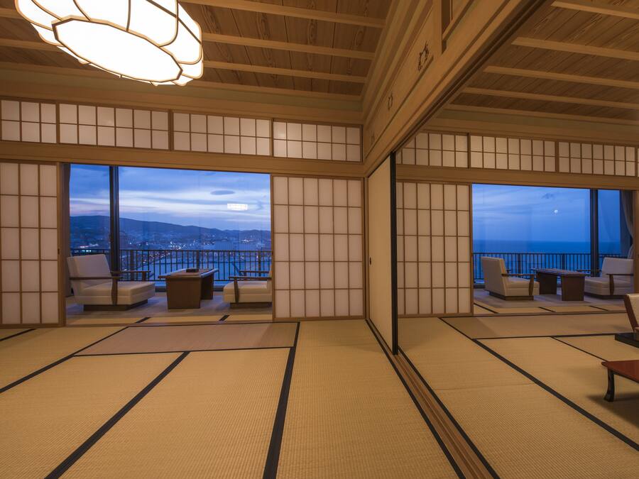 Une pièce de style japonais traditionnel, avec un sol recouvert de tatamis, des portes coulissantes et une vue sur le paysage urbain au crépuscule.
