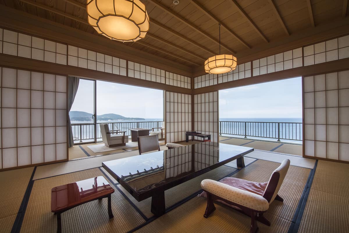 A traditional Japanese room with tatami flooring, a low table, a cushioned bench, and a view of the sea.