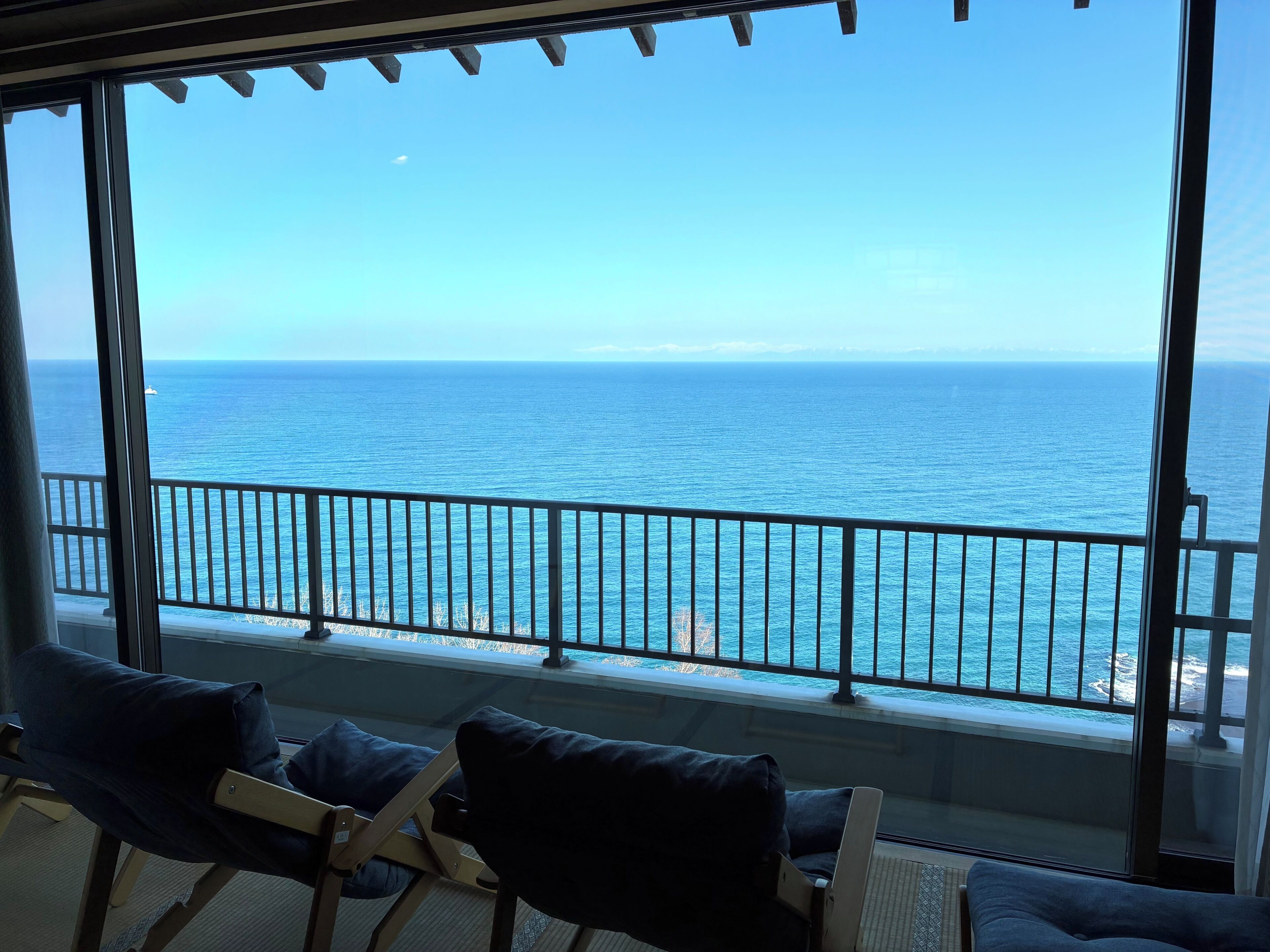 A balcony with a view of the ocean, a railing, and two chairs.