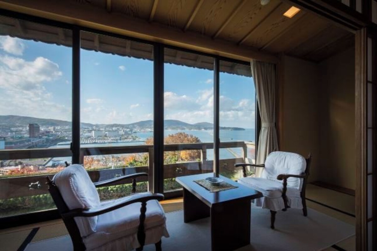 A balcony with a view of a cityscape and hills. There are two chairs and a table.