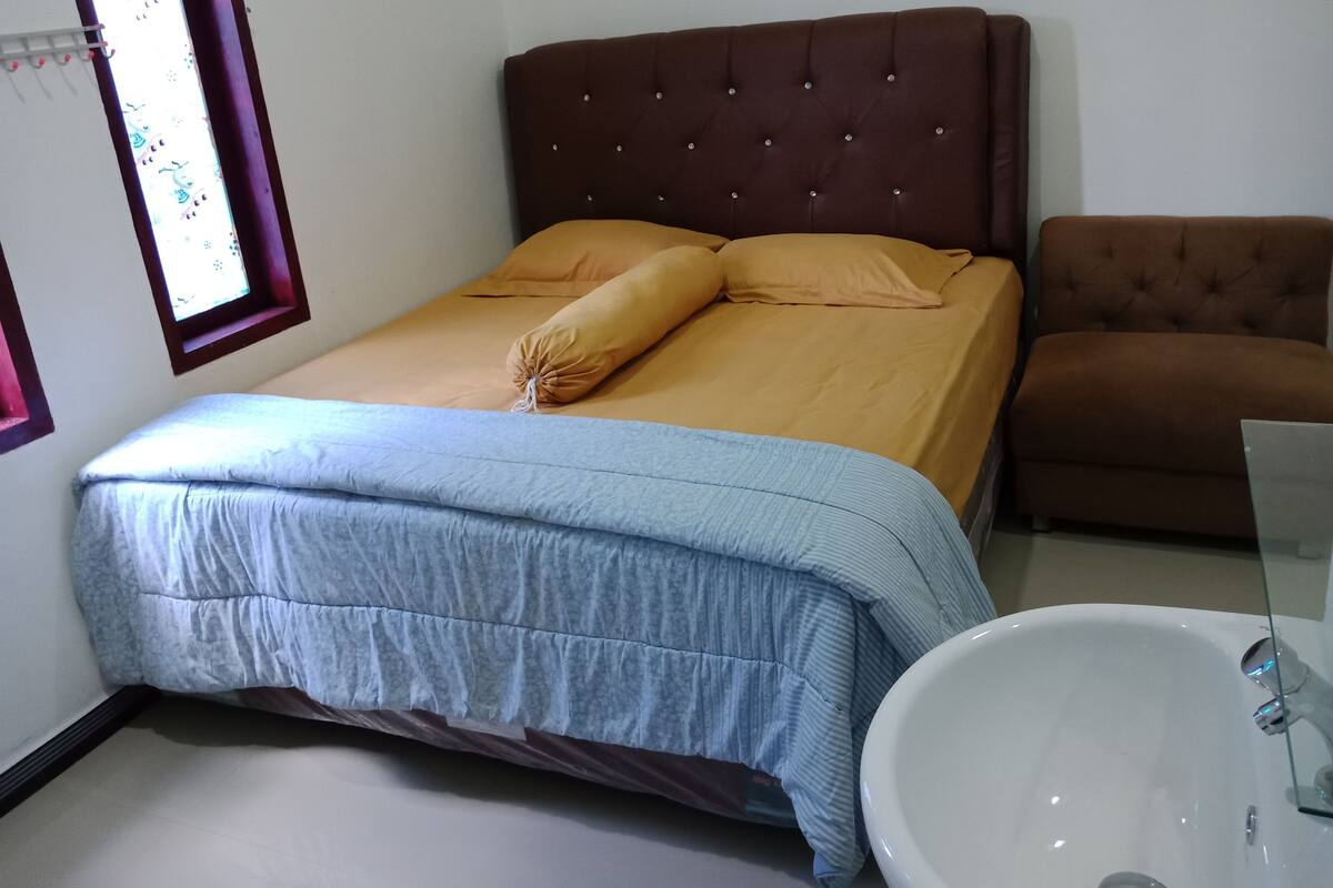 A bedroom with a bed, a brown armchair, and a white sink.