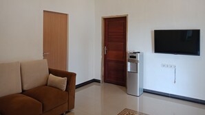 A living room with a brown sofa, a flat-screen TV mounted on the wall, and a water dispenser. - Wakatobi Dive Inn (Kaledupa Island)