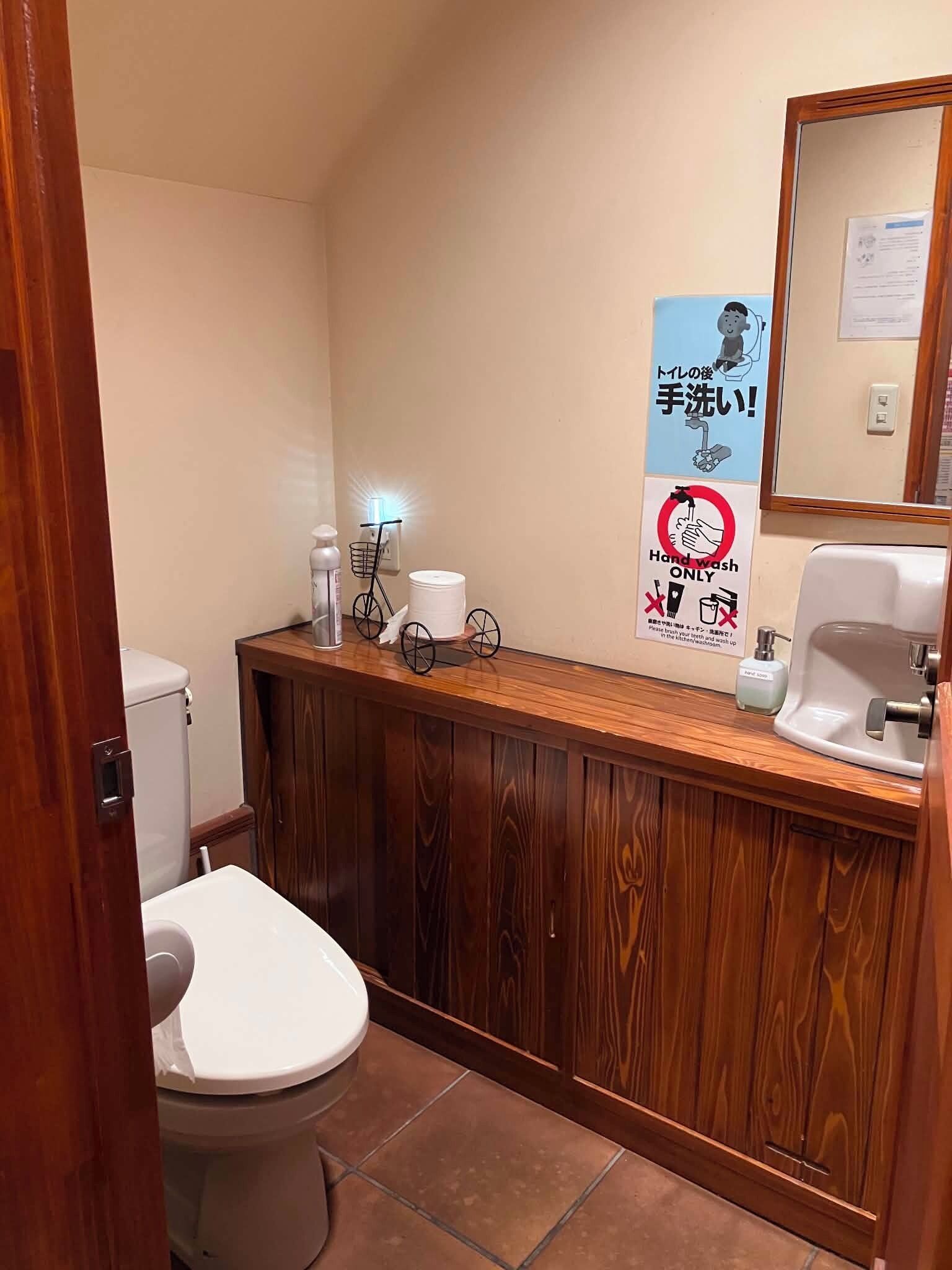 A small bathroom with a toilet, a sink, and a mirror. There are signs on the wall, including one that says 'Hand wash only.'
