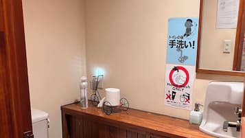 A small bathroom with a toilet, a sink, and a mirror. There are signs on the wall, including one that says 'Hand wash only.'