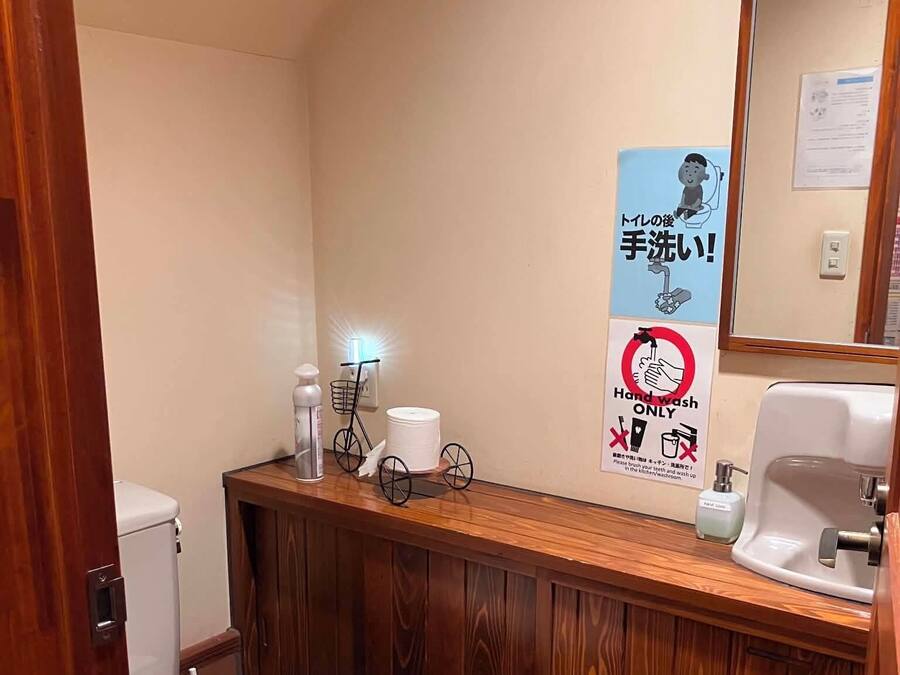 A small bathroom with a toilet, a sink, and a mirror. There are signs on the wall, including one that says 'Hand wash only.'