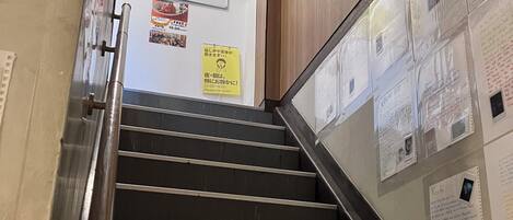 A staircase with metal handrails and wooden steps, leading to a room with a whiteboard and various notices.