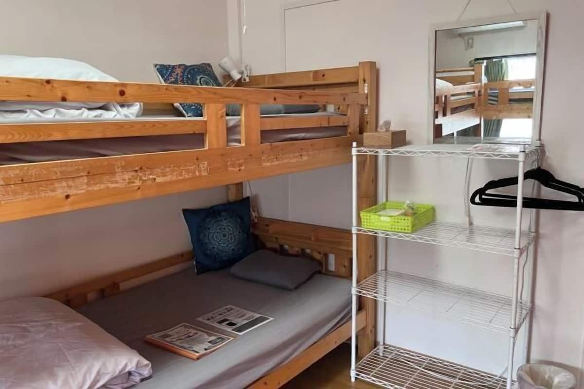 A bunk bed with a lower bunk, a shelf unit with a mirror, and a hanging rack.