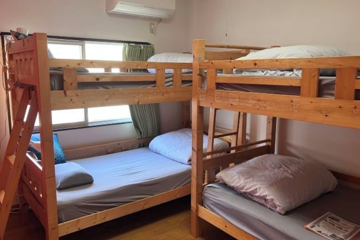 A bunk bed room with a window, a wooden ladder, and a small table.