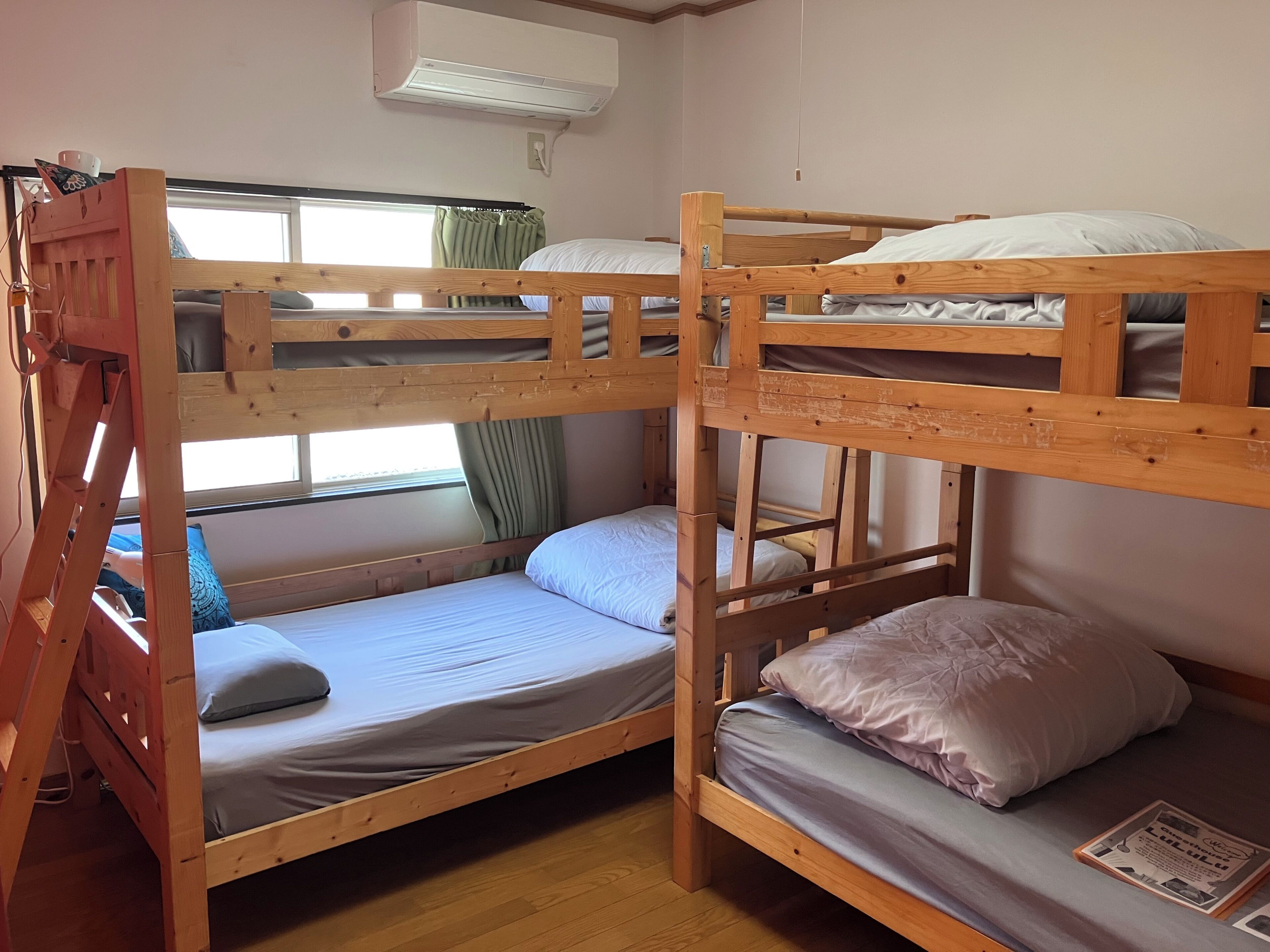 A bunk bed room with a wooden ladder, a window with curtains, and an air conditioning unit.